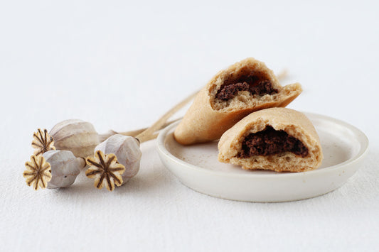 Ein aufgebrochenes süßes russische Pirozhki mit Mohn-Schokoladenfüllung auf einem kleinen Teller neben drei Mohnkapseln