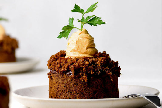 Karottenkuchen-Muffin mit einer Möhre gespritzt aus einer mit Kurkuma gefärbten Sahnecreme und einem Petersilienzweig als Karottengrün