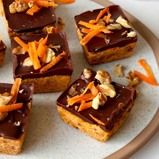 Carrot Cake Bars drappiert auf einem Teller mit Karottenraspel