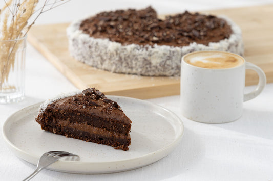 Runder Zucchinikuchen mit einer cremigen Füllung aus Süßkartoffeln, Kakao und Nussmus. Ein Stück steht auf dem Teller vor dem restlichen Kuchen bei einer Tasse Kaffee