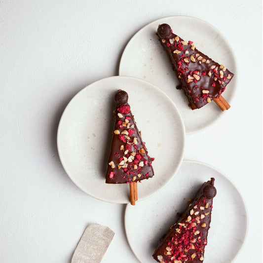 Vegane Gewürzkuchen-Tannenbäume mit Schokolade ummantelt. Von oben auf drei Tellern fotografiert.