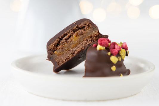 Veganes Sacherplätzen aufgeschnitten auf einem Teller. Man sieht die Schichten im inneren. Außen ist es mit Pistazien und getrockneten Himbeeren verziert