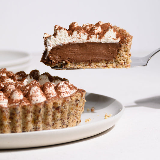 Ein Stückchen vegane Espresso-Schoko-Tarte auf einer Tortenschaufel von der Seite fotografiert. Der Rest der Tarte ist links im Anschnitt zu sehen.
