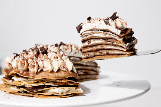 Ein Stückchen vegane Pfannkuchentorte auf einer Tortenschaufel von der Seite fotografiert. Der Rest der Torte ist links im Anschnitt zu sehen.